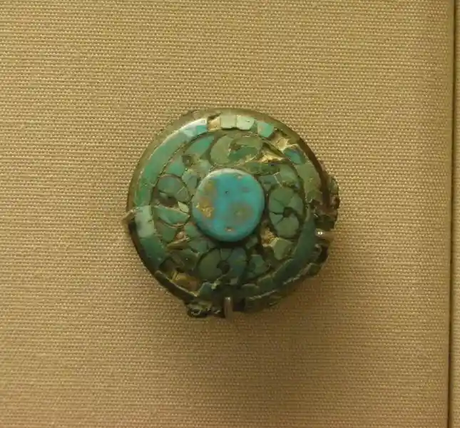 Four swirls around a circle forming a cross on a jade spearhead blade set in a bronze shaft inlaid with turquoise